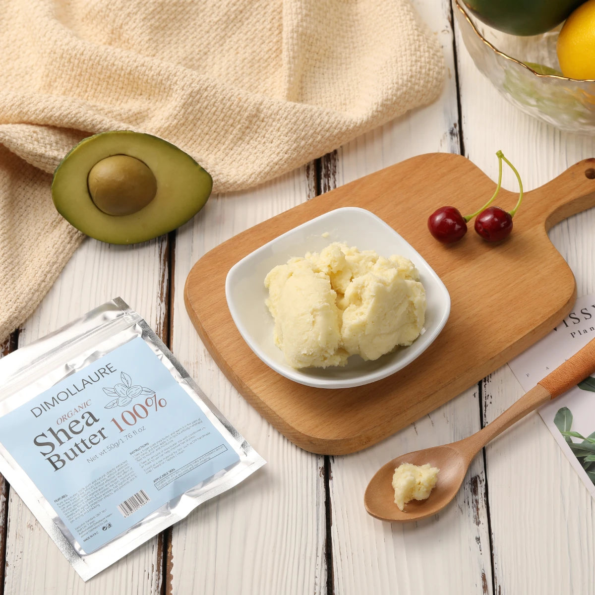 Shea butter on a wooden board with an avocado, cherry, and a package of Dimollaure Shea Butter 100%.