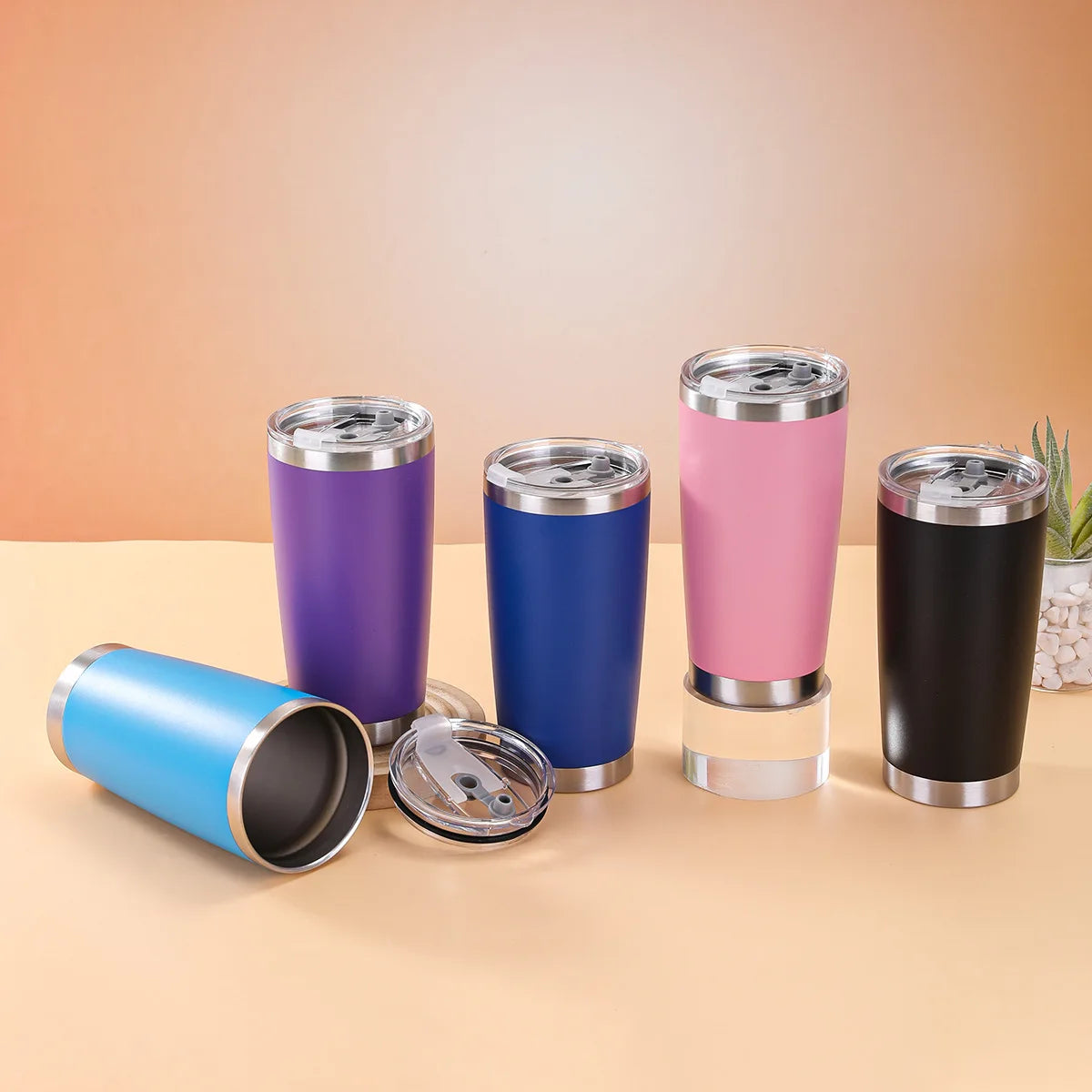 Set of colorful insulated tumblers on a beige surface with a gradient background