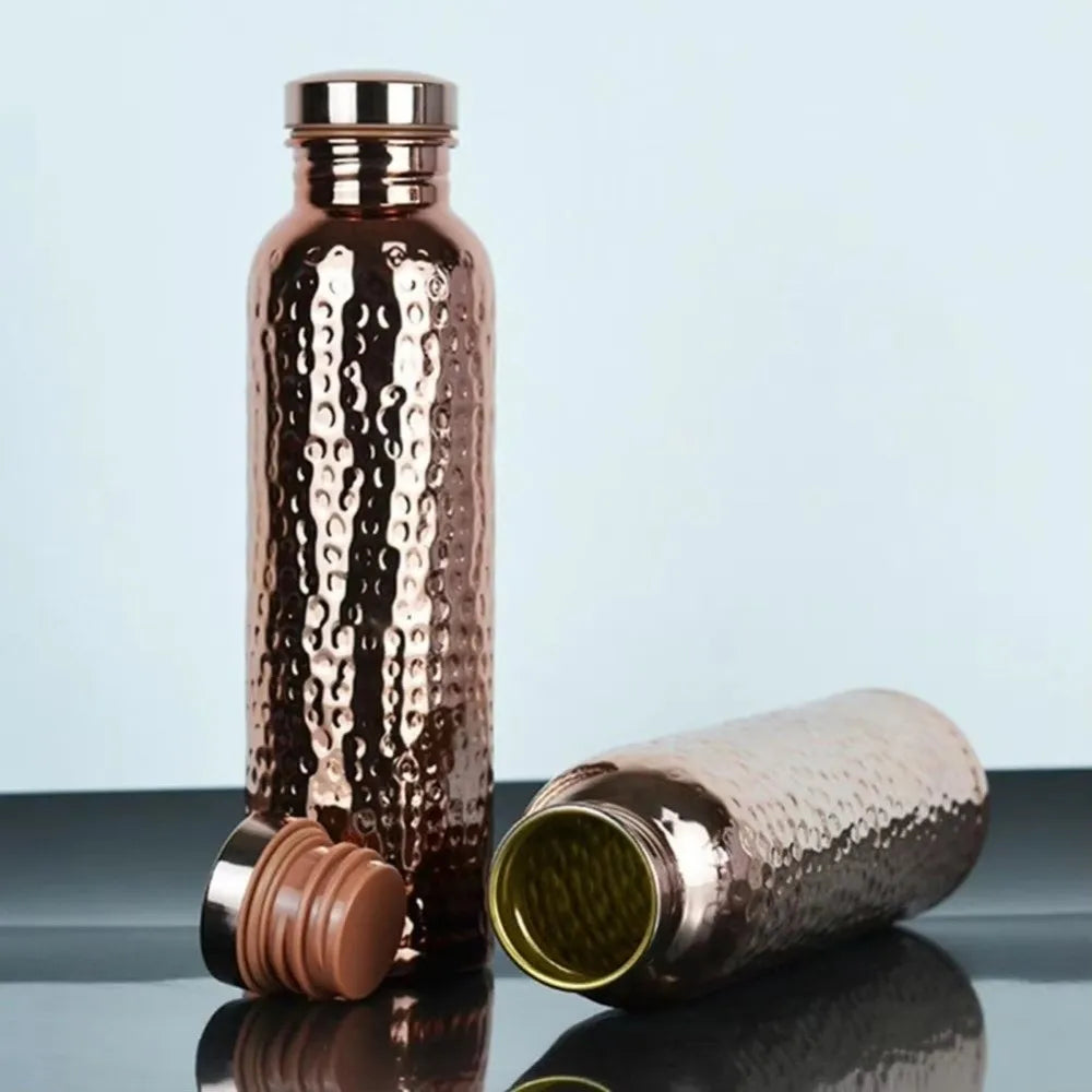 Copper water bottles with a textured surface on a reflective surface with a light blue background