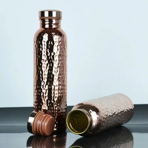 Copper water bottles with a textured surface on a reflective surface with a light blue background