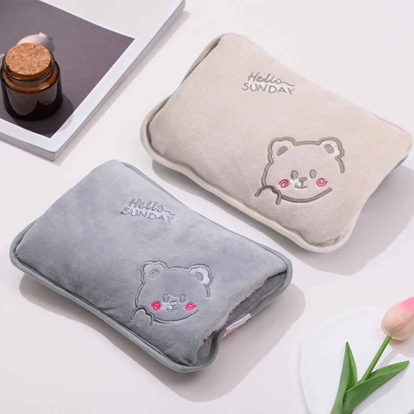 Two hot water bottles with bear designs and 'Hello Sunday' text on a light surface.