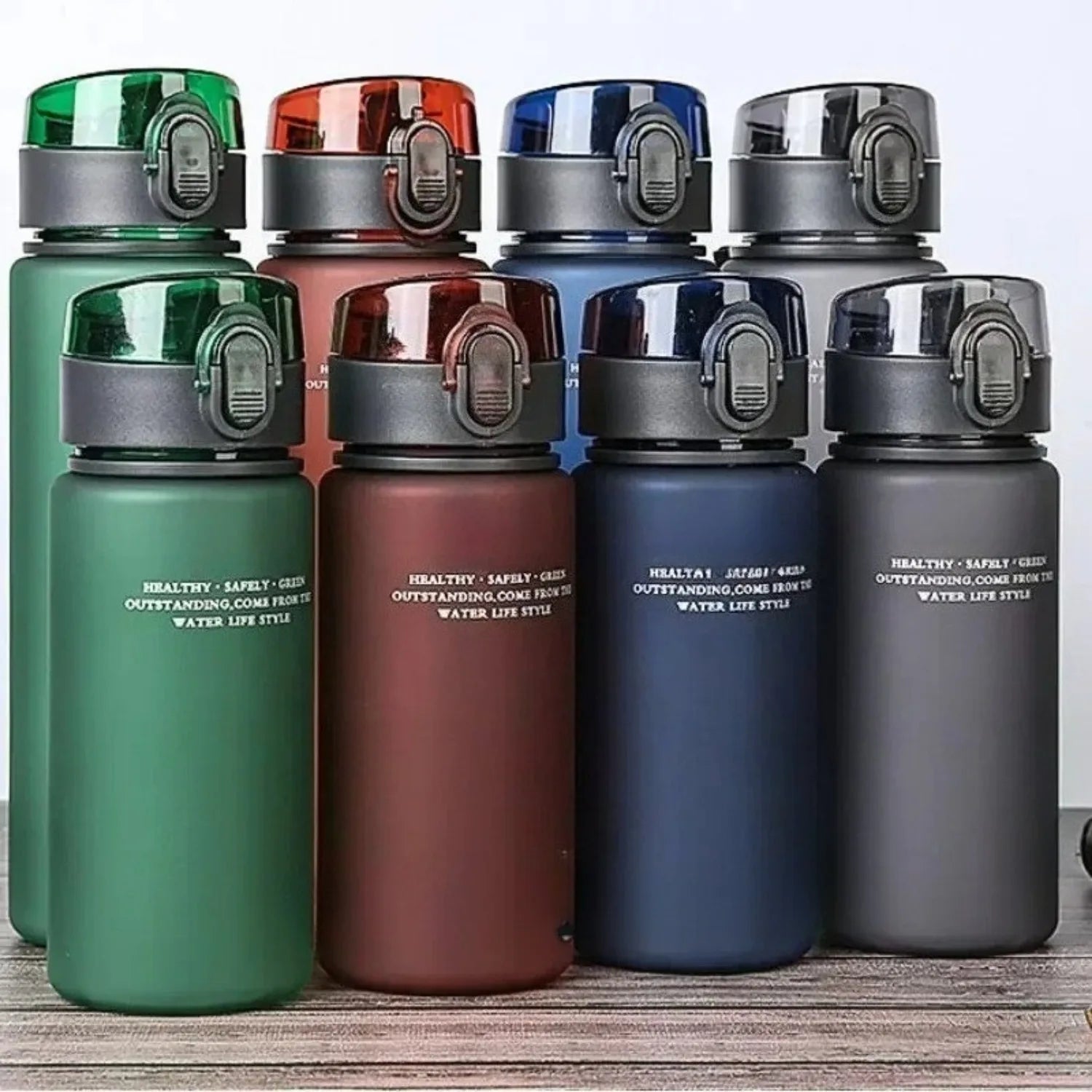 Set of four water bottles in green, red, blue, and gray on a wooden surface.