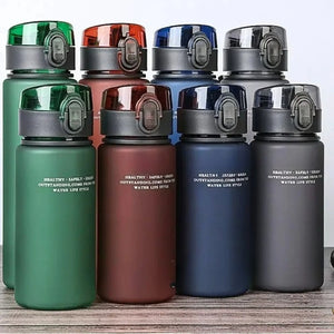 Set of four water bottles in green, red, blue, and gray on a wooden surface.