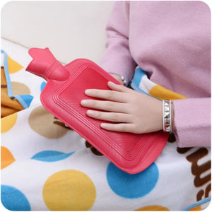 Person holding a pink hot water bottle on a colorful blanket